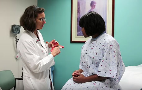 A female doctor holding a model of a uterus and explaining someting about it to a seated patient.