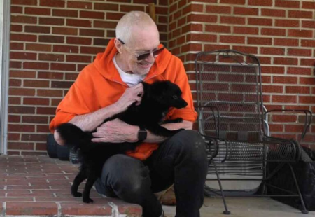 Man who underwent open aortic aneurysm repair happily pets dog in front of building 